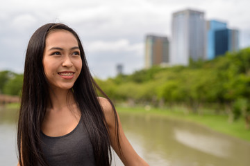 Young beautiful Asian woman smiling and thinking at the park