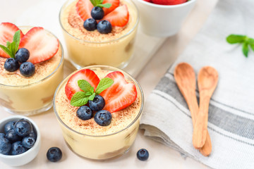 homemade, exquisite dessert tiramisu in glasses decorated with strawberry, blueberry, mint on white wooden table, top view.