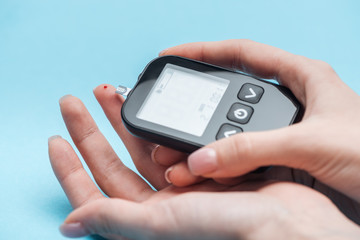 cropped view of woman testing glucose level with glucometer on blue background