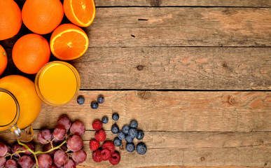 Naklejka na ściany i meble View from above of jug with orange juice, fresh oranges, apples, grapes, raspberries and blueberries on a wooden table - fruit background