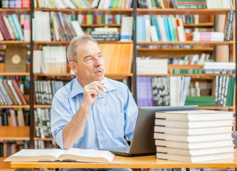 Pensive old man in the library. Empty space for text