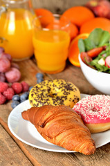 Obraz na płótnie Canvas Close-up of croissant and donuts, orange juice and fresh salad - breakfast on wooden table vertical photo
