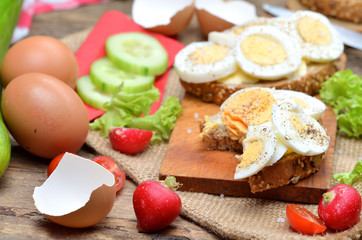 Wholegrain bread with butter, hard-boiled eggs, fresh radishes, tomatoes, salad and cucumbers in background