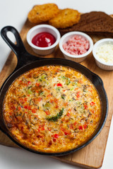 Frittata on a skillet with sauces and bread