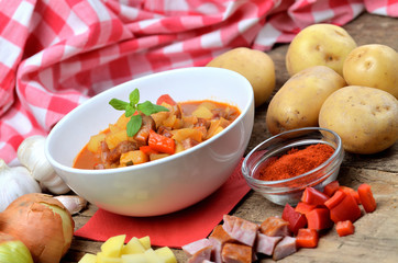 Potato and sausage goulash, pepper, onion and garlic on wooden table