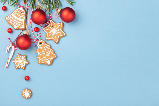 Gingerbread cookies with red Christmas balls and candy cane lollipop hanging over blue background and decorated with berries and rosemary. Top view, copy space.