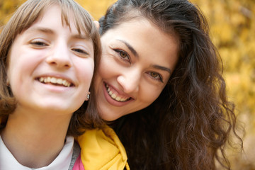 Portrait of pretty woman and teen girl. They are posing in autumn park. Beautiful landscape at fall season.