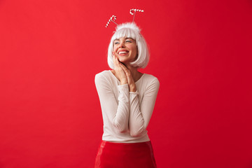 Young happy woman dressed in carnival christmas costume posing isolated over red wall background.