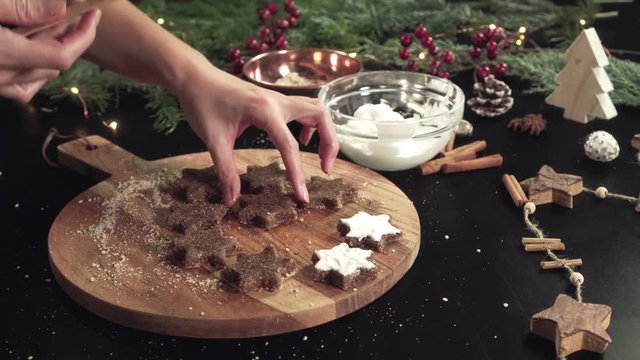 Putting the topping onto Zimtsterne (Cinamon Stars) on a rustical wooden cutting board with christmas decoration around it