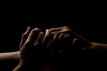 Hands of the old mother and young daughter on a dark background