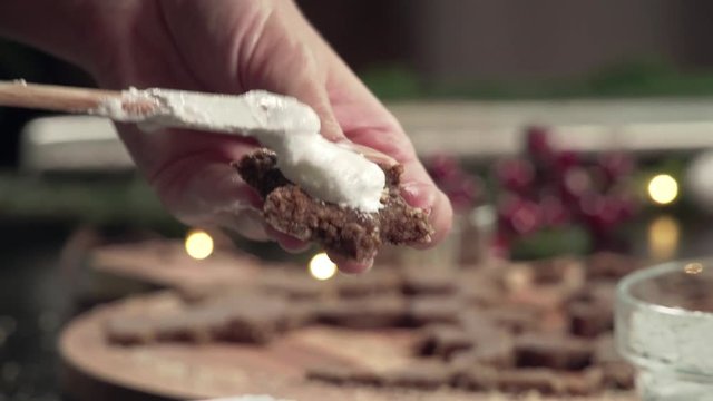 Putting the topping onto Zimtsterne (Cinamon Stars) on a rustical wooden cutting board with christmas decoration around it