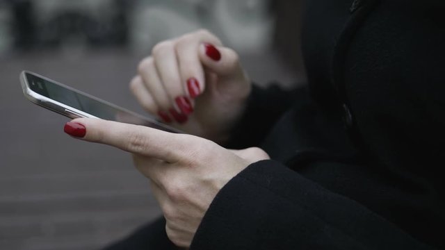 Woman's hands using smartphone touchscreen at cold season outdoors.