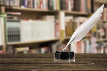 Feather quill pen and glass inkwell on library background