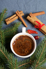 Obraz na płótnie Canvas A cup of coffee on the table. Cinnamon sticks and pods of red pepper next to the fir branches. On a woven background.
