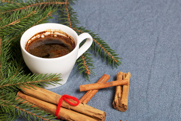 Obraz na płótnie Canvas A cup of coffee on the table. Cinnamon sticks next to the fir branches. On a woven background.