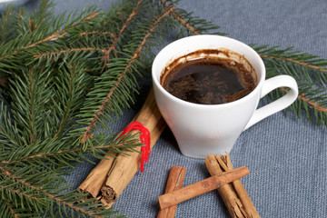Obraz na płótnie Canvas A cup of coffee on the table. Cinnamon sticks next to the fir branches. On a woven background.