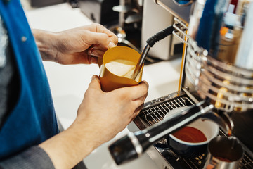Close up of barista steaming milk in the pitcher with coffee machine.
