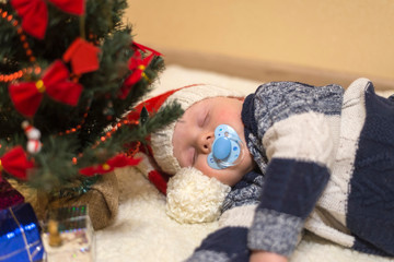 Little baby with nipple in Santa's hat sleeping under the Christmas tree
