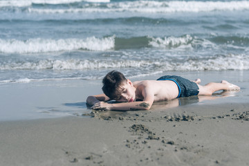 Happy teen boy sleeping on the sand оn the beach 