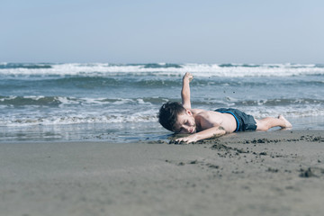Happy teen boy having fun training or imitates swimming on the sand оn the beach 