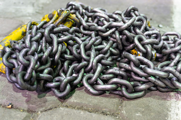 Chains made of iron with hooks of yellow color, for raising a large load, lie on the floor in the production workshop. Abstract industrial background.