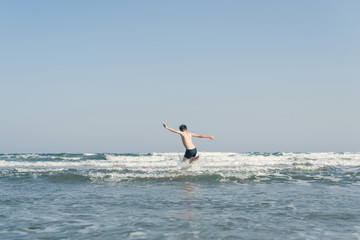 Fototapeta na wymiar Boy Jumping In Sea Waves with Water Splashes. Concept of summer vacation