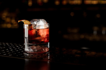 Glass of a Boulevardier cocktail with orange zest on the steel bar counter
