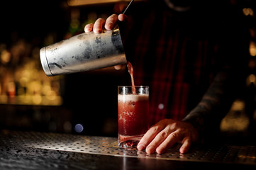 Fototapeta na wymiar Bartender pouring a delicious Sippy Cup cocktail from the steel shaker