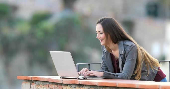 Happy Woman Typing On A Laptop In A Rural Apartment Balcony