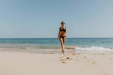 Portrait of happy smiling woman in bikini walking on the beach.