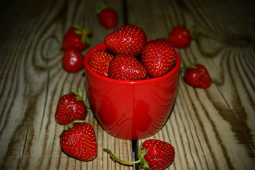 Fresh strawberries in a cup on wood background