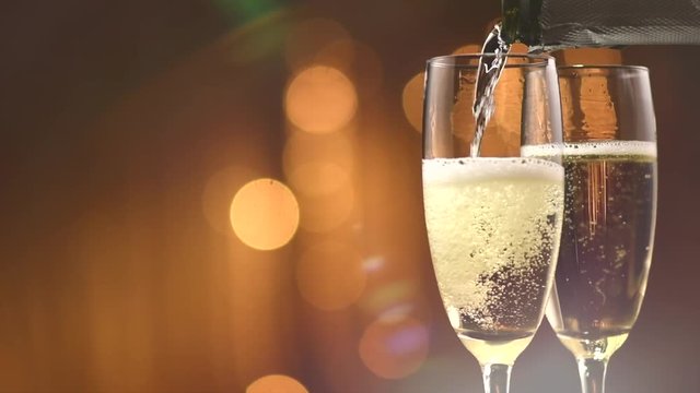 Champagne pouring from a bottle. Two flutes with sparkling wine over golden holiday bokeh blinking background. Celebration. Slow motion 4K UHD video footage. 3840X2160