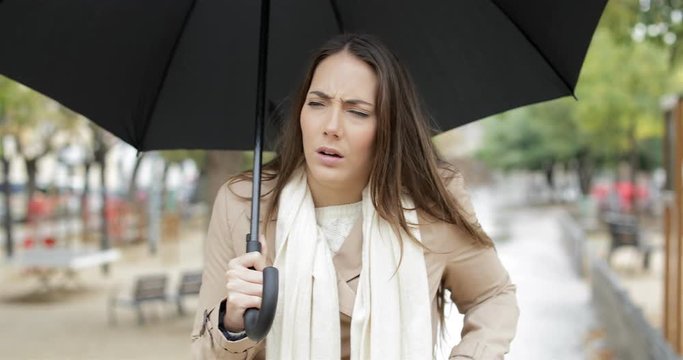 Front view of an ill woman walking towards camera sneezing walking under the rain holding an umbrella in a park
