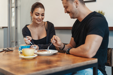 Young couple sitting in cafe at date, drinking coffee and eating dessert.