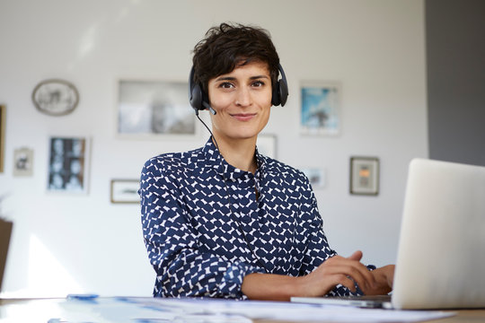 Portrait of smiling woman at home with headset and laptop
