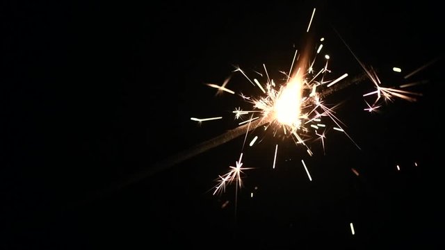 Bright burning sparkler on deep black background closeup. Sparklers holiday backdrop. Christmas or New Year background. 4K UHD video footage. Slow motion 3840X2160