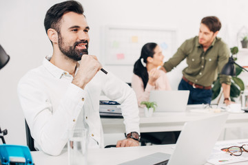thoughtful office manager sitting in office with coworkers on background