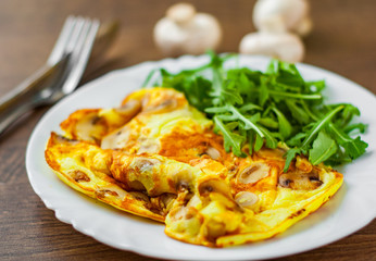 Omelet with mushrooms and arugula salad in white plate on wooden table background.