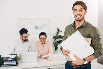 Selective focus of young manager standing with folders in office