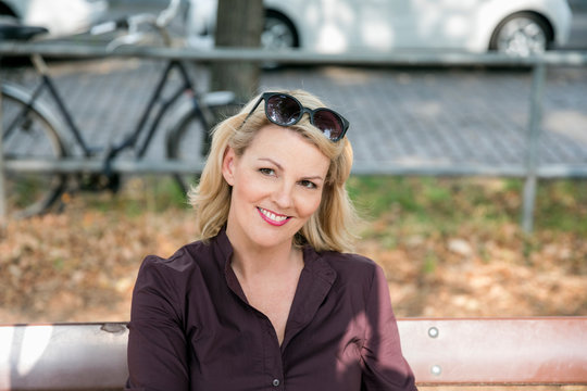 Portrait of smiling blond mature woman sitting on bench outdoors