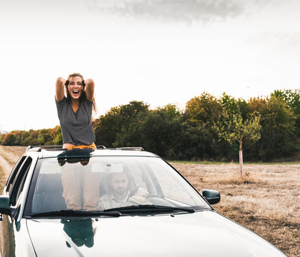 Carefree young woman looking out of sunroof of a car