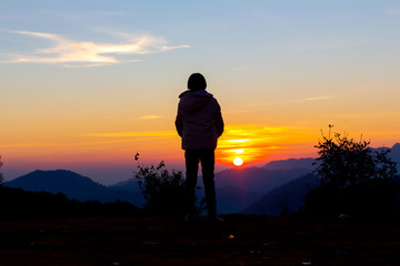 Silhouettes of young girl looking morning sunrise on peak of mountain.