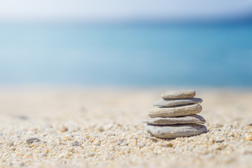Fototapeta na wymiar Vertical ordered stones on sand at the beach. Blurred blue sea at background