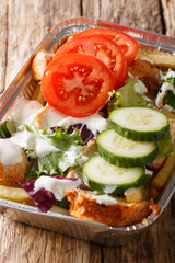 Kapsalon from the Netherlands: french fries topped with shawarma meat, then Gouda cheese and fresh vegetables closeup. vertical