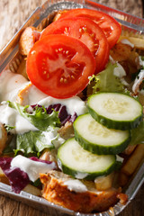 Dutch fast food kapsalon of french fries, chicken, fresh salad and sauce close-up in a foil tray. vertical