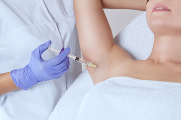 The doctor makes intramuscular injections of botulinum toxin in the underarm area against...