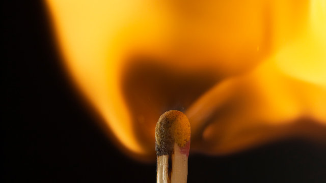 Burning wooden match with a red match head on a black background.