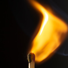 Burning wooden match with a red match head on a black background.