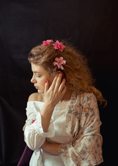 Fototapeta premium Portrait of a young romantic woman with blond curly hair in a vintage floral dress sitting over black background. Close Up of woman