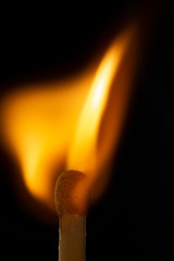 Burning wooden match with a red match head on a black background.